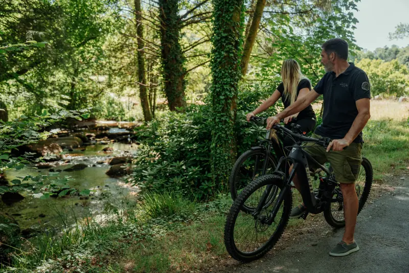 Deux cyclistes en vélo électrique longent la rivière d'Argent dans la forêt de Huelgoat